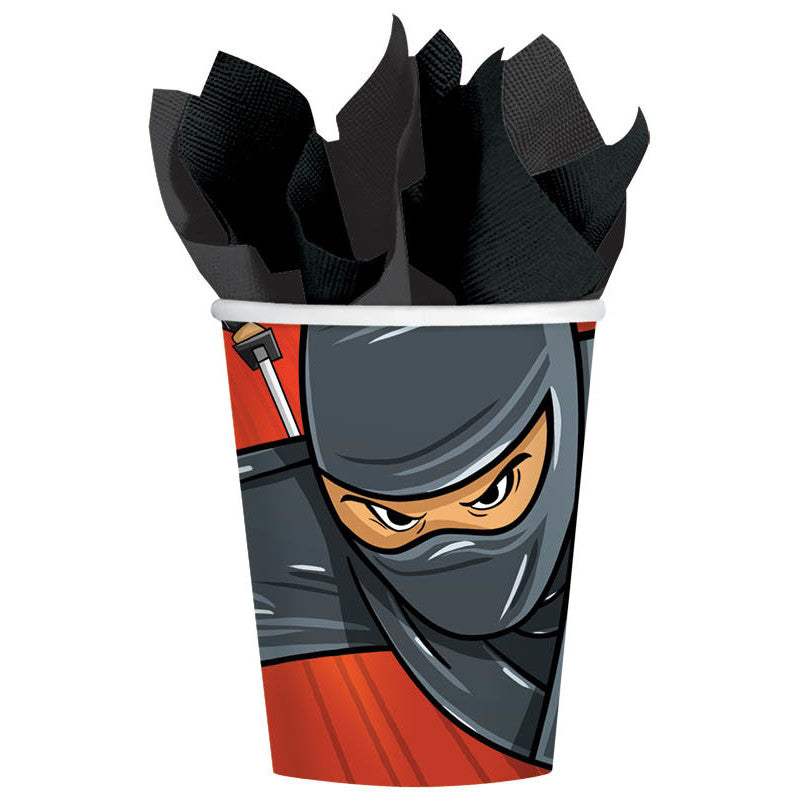 Amscan's Ninja Cups ( 8 ct. ) decorated with a licensed cartoon image of a ninja in black and red attire, with intense eyes visible through a mask. The cups are filled with black napkins resembling the ninja's attire.
